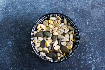 Sunflower and pumpkin seeds in bowl on the blue background. Large group of seeds. Snack and...
