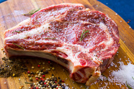 Raw spiced beef meat on the table, spices and Rosemary, Rib eye steak ingredients. Pepper and coars...