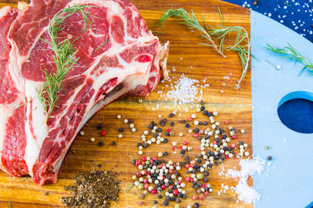 Raw beef meat on the table, spices and Rosemary, Rib eye steak ingredients. Pepper and coars salt....