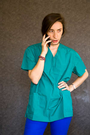 Woman portrait in medical nurse and doctors uniform on the gray background, woman talking on the mobile phoneの写真素材
