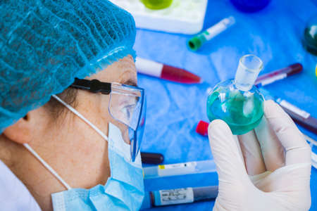 Doctors in uniform, face mask and glasses looking at sample in laboratory, colorful liquid chemical...
