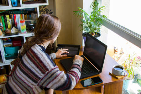 Tbilisi, Georgia - October 09, 2020: Woman working with notebook in workplace, digital tablet, mobile phone, coffee and plants in workspace, home workingの写真素材