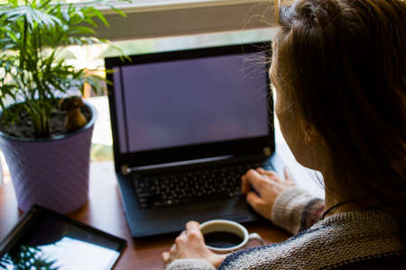 Woman working in office with digital tablet and notebook, writing and typing on the deviceの写真素材