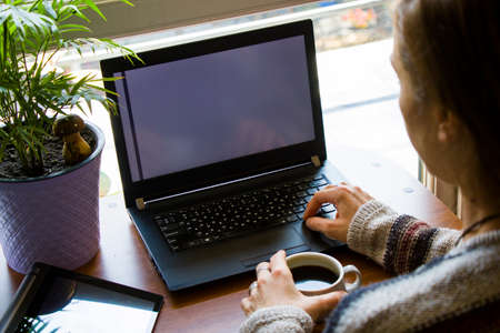 Woman working with notebook in workplace, digital tablet, mobile phone, coffee and plants in...