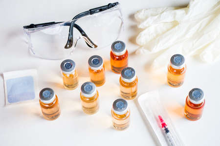 Vaccine in ampules and bottles, needle, glove and safety glass.の写真素材
