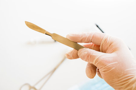 Surgery knife holding on the white background, studio shot. Operation equipment. White glove.