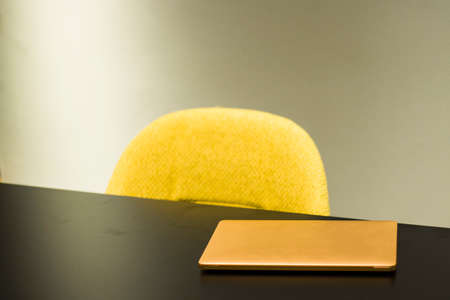 Laptop and notebook on the black table and yellow chair in office, no people