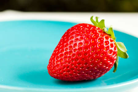 One strawberry on the blue background, raw real strawberry, ready to eatの写真素材