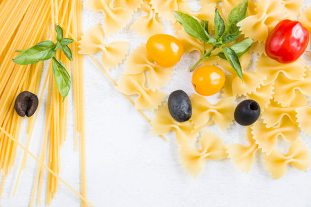 Pasta ingredients, raw pasta, cherry tomatoes, olives and basil leaves on the white background