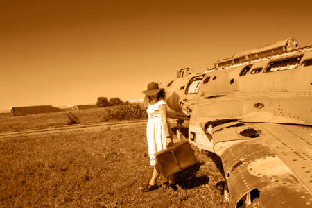 Beautiful women with red hat, sunglasses and suitcase near old and abandoned Soviet union army jet