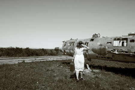 Beautiful women with red hat, sunglasses and suitcase near old and abandoned Soviet union army jet