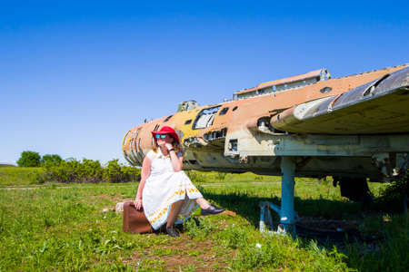 Beautiful women with red hat, sunglasses and suitcase near old and abandoned Soviet union army jet