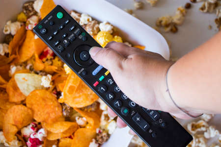 Fried popcorn and chips in bowl on the white background, hand holding TV controller, low angle view