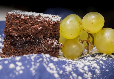 Chocolate sponge cake with icing sugar and grapes on the blue tablecloth.の写真素材