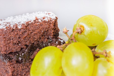 Chocolate sponge cake with icing sugar and grapes.の写真素材