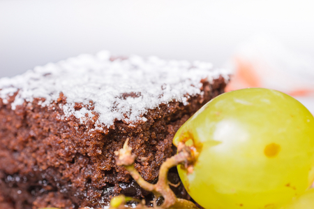 Chocolate sponge cake with icing sugar and grapes.の写真素材