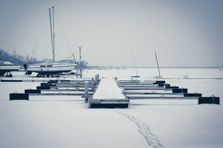 Sailboats moored in foggy harbor. Cold winter landscape with snow and iceの写真素材