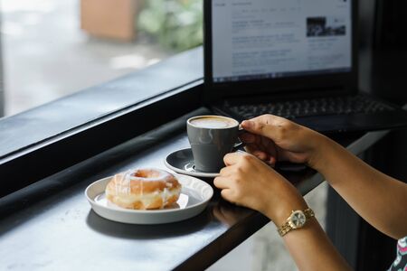 A girl holds a hot latte cup with a donut beside her.の写真素材