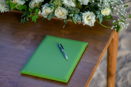 Green notebook and pen on a wooden table with a bouquet of flowersの写真素材
