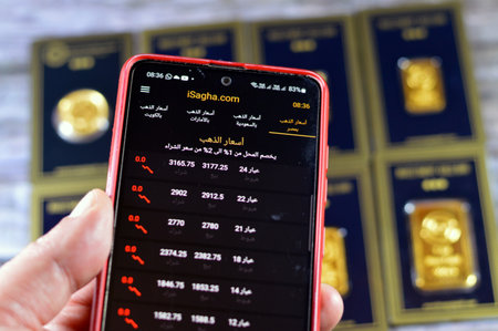 Cairo, Egypt, December 8 2023: Isagha gold price in Egypt, Saudi Arabia, Kuwait and United Arab Emirates, Isagha application for gold prices, with gold bars in the background, saving assets conceptのeditorial素材