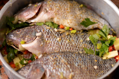 tilapia fishes Oreochromis niloticus mixed with slices of tomatoes, potatoes, carrots, celery, onion, spices, cumin, black pepper and salt, in a tray and ready to be baked in the oven, selective focusの写真素材