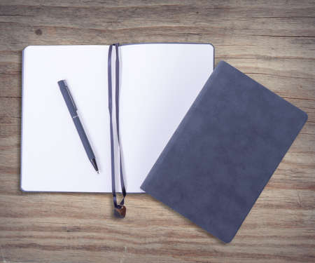 open and closed gray plain velveteen notebooks and gray metal pen on wooden desk. Over viewの写真素材