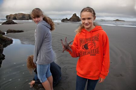 Gold Beach, Oregon, August 14 2010: A smiling young girl holds a starfish that she discovered while walking on the beach with her sister and mother.のeditorial素材