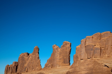 The effects of erosion over time have shaped this massive sandstone wall which stands against the dramatic blue Utah sky in Arches National Park.の写真素材