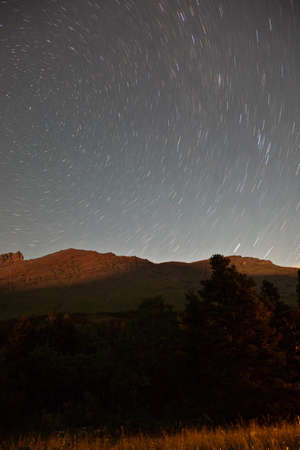 A long exposure nighttime mountain landscape in Glacier National Park, illuminated by moonlight with...