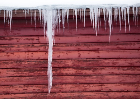 A giant icicle hangs down the side of a red wood barn with other icicles along the eaves.の写真素材