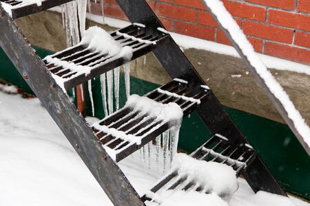 Black metal stairs with icicles hanging underneath the middle of each grated platform and snow on top.の写真素材
