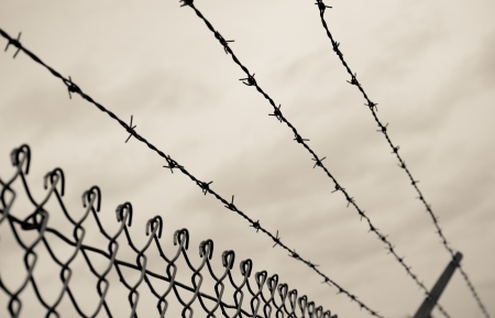 Three rows of barbed wire on top of a chain link fence with an aged photo look.