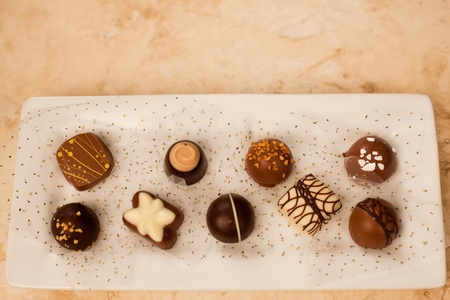 Hand made artisan chocolates nestled in gold glitter netting on a white plate with a marble counter...