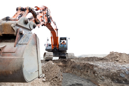 A construction worker operating a track hoe machine that is sitting on dirt with an isolated sky background.の写真素材