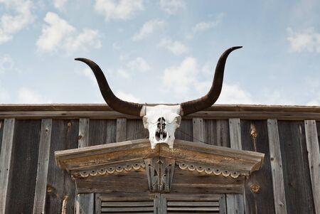 The skull of a Texas longhorn cow is hung above an entrance way of an old western wooden building.の写真素材