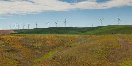 Rolling hills and green farmland provide a perfect ridge for giant windmills to stand on and create green energy.の写真素材