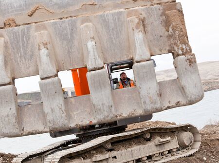 A creative view through the open grate of a bucket on a track-hoe machine to view the male operator...