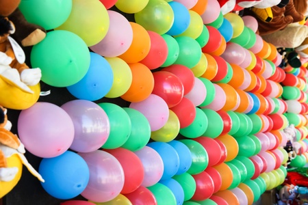 A shinny red balloon stuck into rows of balloons in various colors on a wall for a dart throwing game at a fair.の写真素材