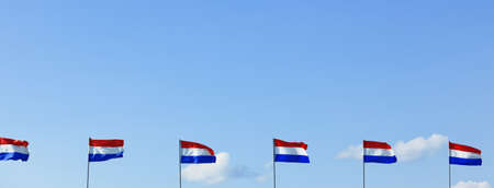 A row of red white and blue vertically striped flags wave in the wind with a blue sky background.の写真素材