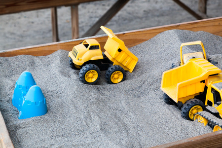 A bright yellow dump truck plastic toy in a raised wooden sand box with other plastic toys around...