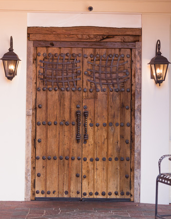 Antique wooden doors banded by hammered ironwork with lanterns on either side.の写真素材