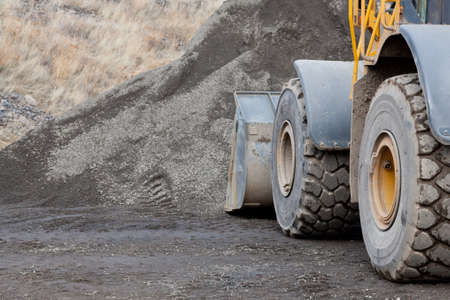 Large wheels and the bucket of a construction loader up against a pile of gravel at a job site.