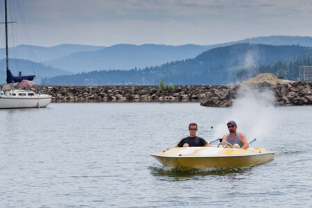 Two me in a small speedboat going slow through a now wake zone in a marina.の写真素材
