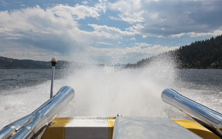 Water spraying up in the wake of a fast yellow and white speedboat on Lake Coeur d'Alene, ID.