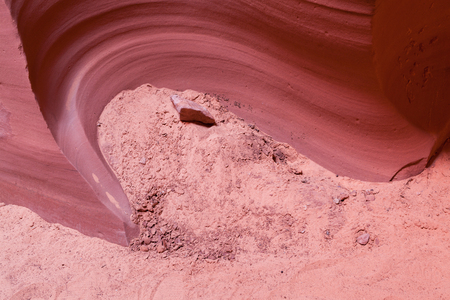Sand and rock at the base of a sandstone wall that has been carved out by erosion to create a swirled feature.の写真素材
