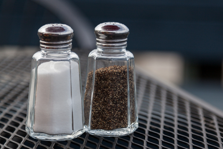 Glass salt and pepper shakers on an outdoor table top at a restaurant.