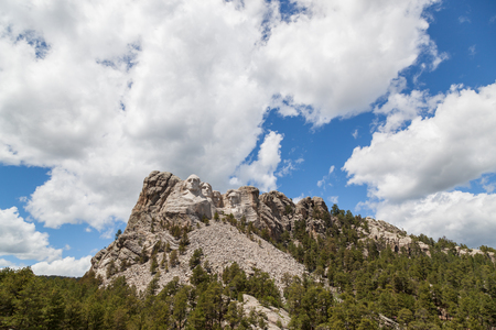 Sunshine, blue sky and white clouds provide a striking back drop for the carved faces of four famous United States Presidents in Mount Rushmore National Memorial.のeditorial素材