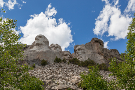 Blue sky and white fluffy clouds provide a striking back drop for the carved faces of four famous United States Presidents in Mount Rushmore National Memorial.のeditorial素材