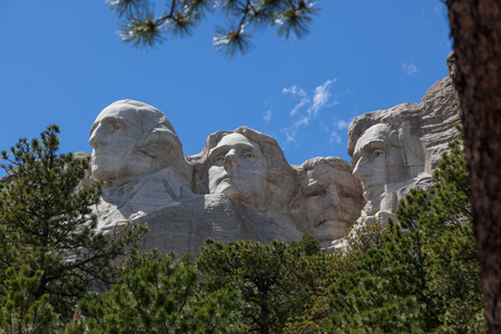 Sunshine, blue sky and white clouds provide a striking back drop for two of the carved faces of famous United States Presidents in Mount Rushmore National Memorial.のeditorial素材