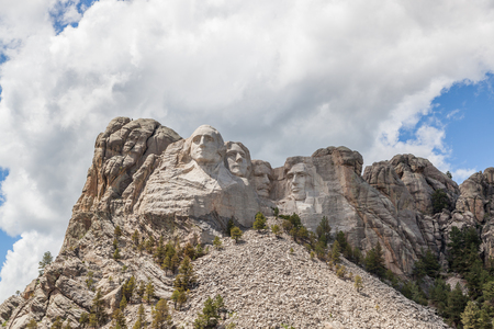 Sunshine, blue sky and white clouds provide a striking back drop for two of the carved faces of famous United States Presidents in Mount Rushmore National Memorial.のeditorial素材